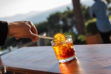 Hand garnishing a drink with an orange slice.